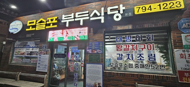 밤에 불이 켜진 모슬포 부두식당 간판과 가게 입구